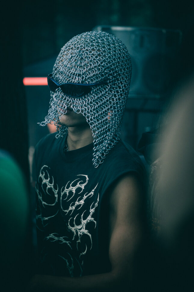 A man with a chainmail mask, sunglasses and sleeveless shirt with death metal graphics dances in the early morning hours of Sustain-Release at the Grove.