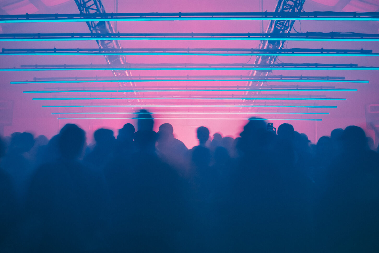 Surreal image of silhouettes of people dancing with a grid of parallel neon lights hangs above their heads at the main stage of Sustain-Release.