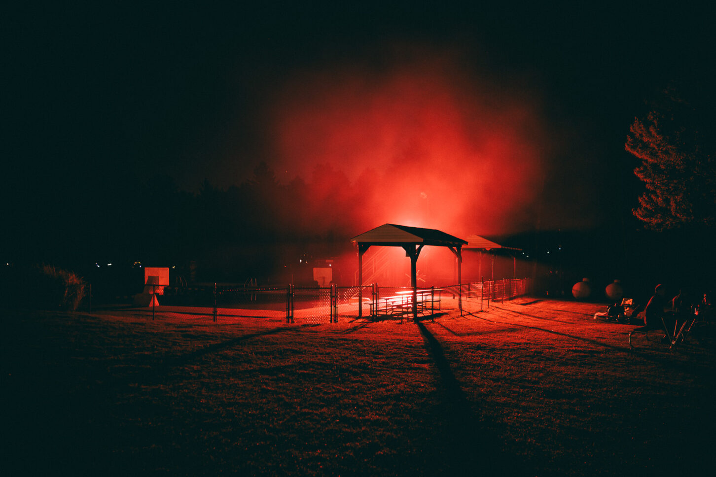 Night shot of the pool pavilions of Camp Kennybrook during Sustain-Release with fog in the background and a bright red light illuminating the scene.