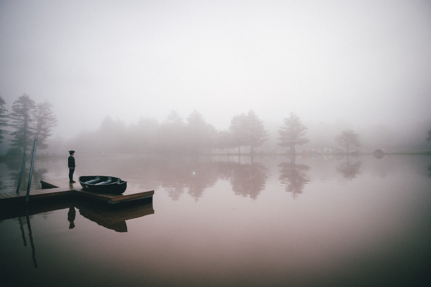 Landscape photo of a girl standing on a T-shaped dock on a foggy morning at Camp Kennybrook during Sustain-Release.
