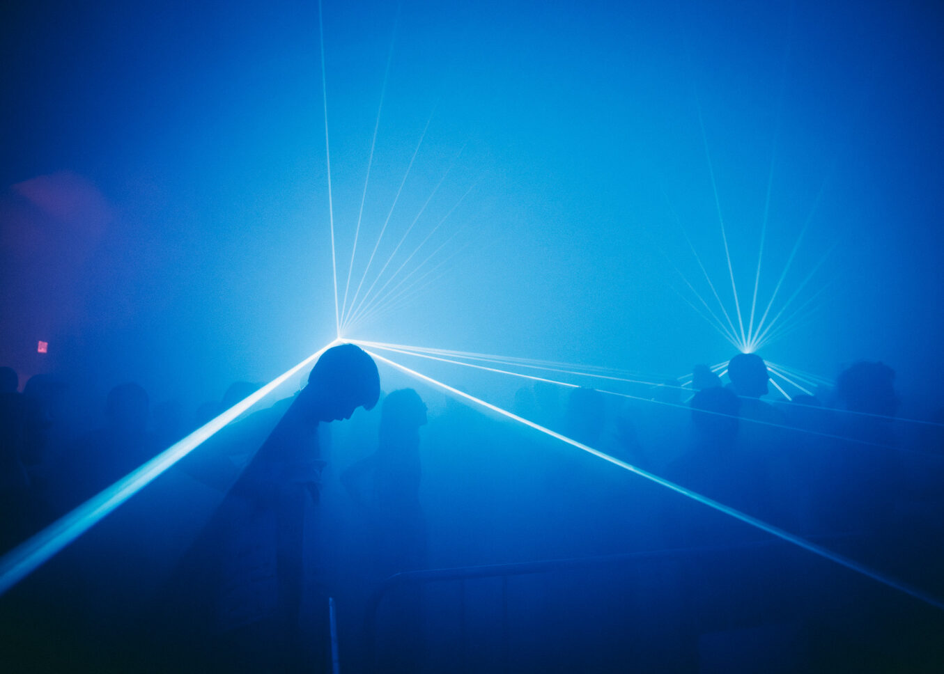Blue silhouettes of people on the dance floor of Sustain-Release with streaks of light emanating from their heads.