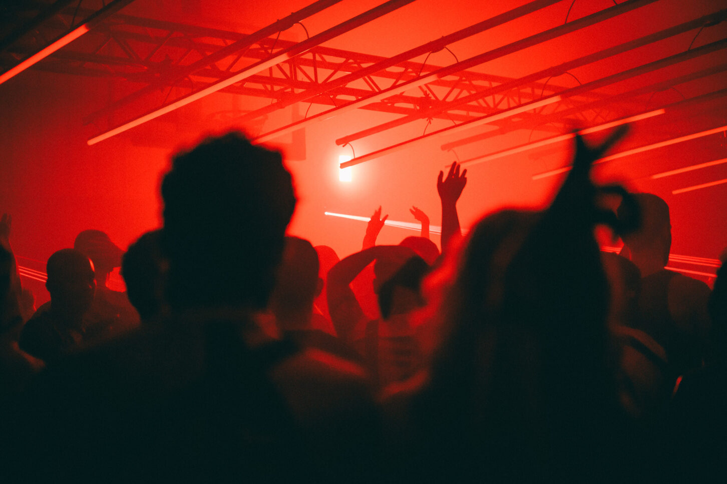 Silhouettes of people dancing under a red light at Sustain-Release main stage.