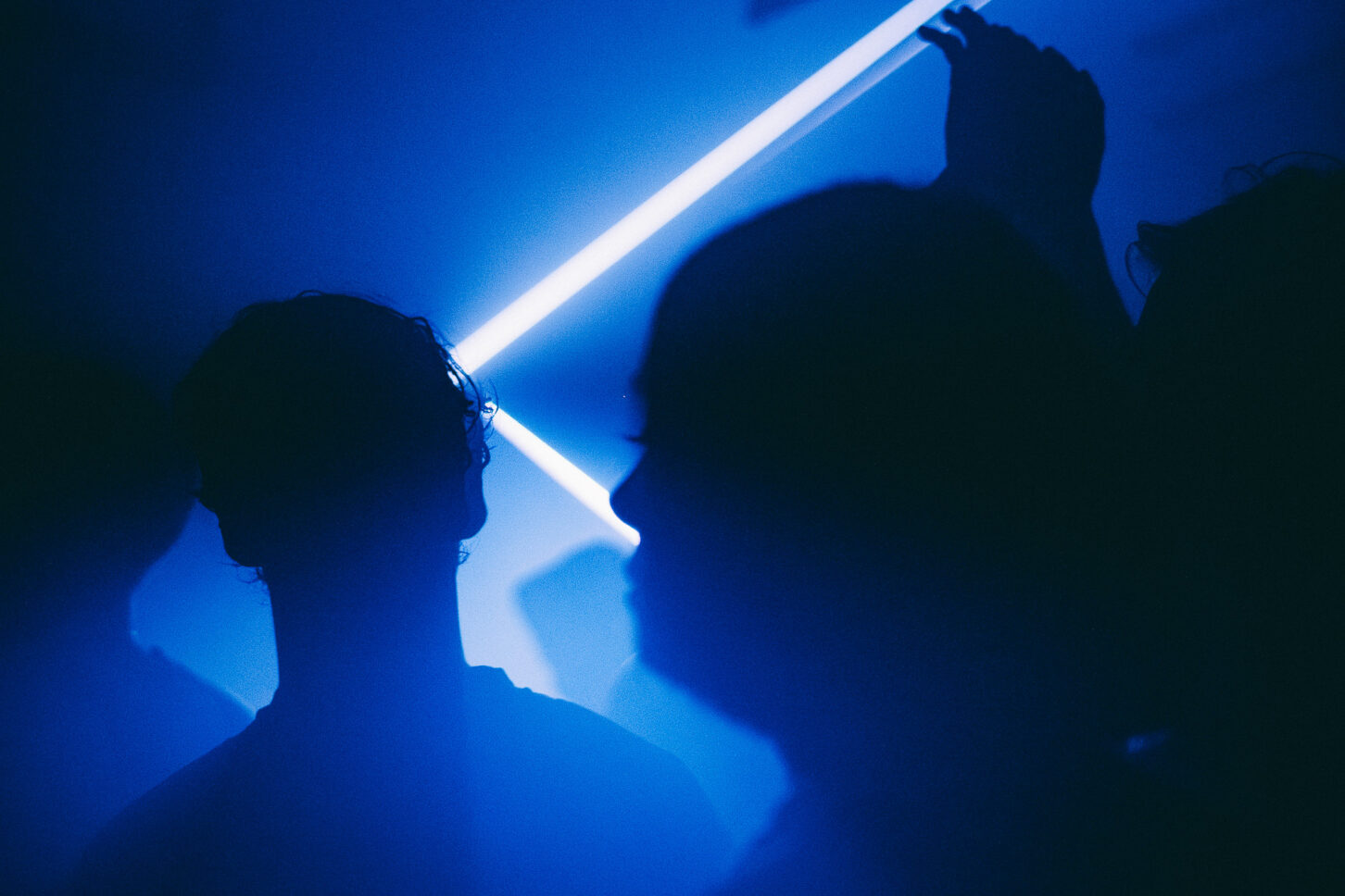 Dark silhouettes of people dancing under the blue lights and lasers of Sustain-Release.
