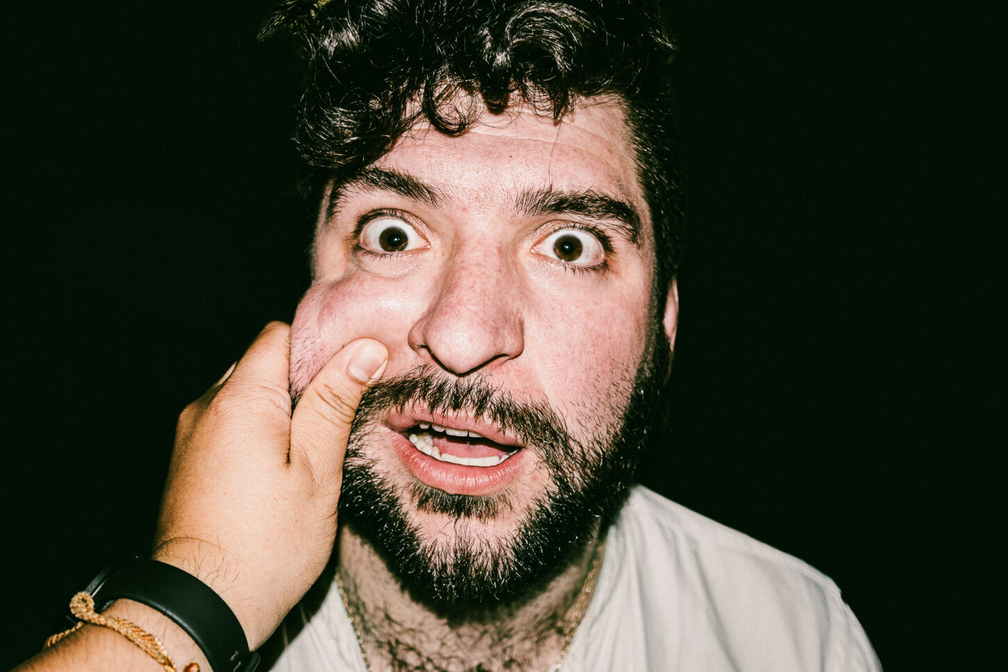 A person with an exaggerated, playful look of shock in a close-up flash portrait, highlighting the raw human narrative of the 'Cheeky Bastards' series.