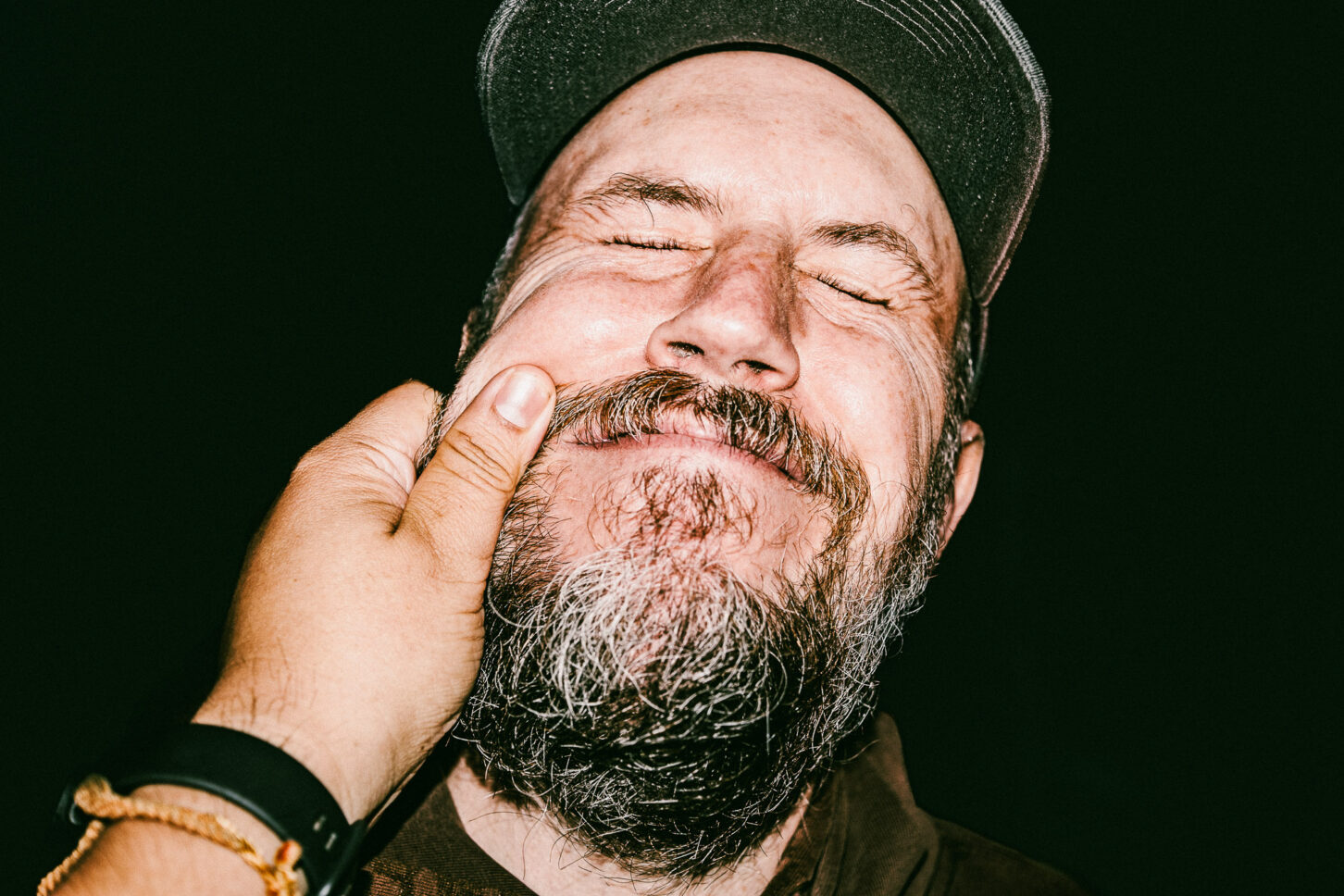 A person with a "painfully funny" grimace, eyes squeezed shut, in a raw flash portrait reacting to the 'Cheeky Bastards' pinch.