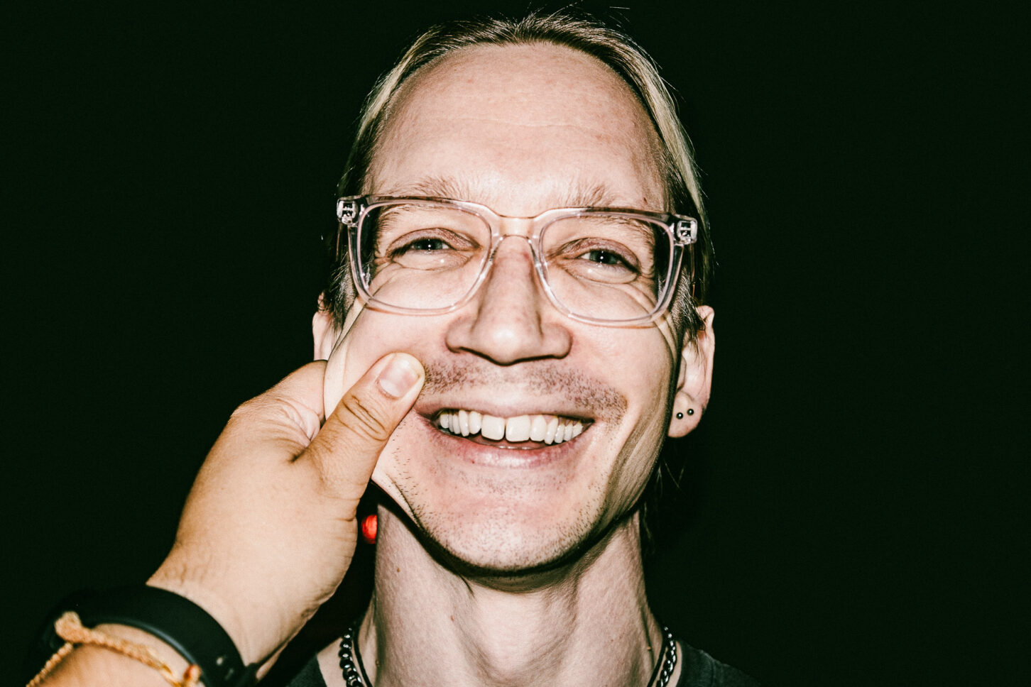 A person looking directly into the lens with an intense, wide-eyed stare while their cheek is pinched, highlighting the raw energy of the 'Cheeky Bastards' series.