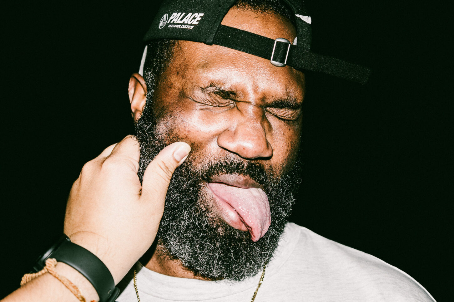 A moody, high-contrast shot of a subject looking down while enduring a cheek pinch, adding a different tone to the 'Cheeky Bastards' series.