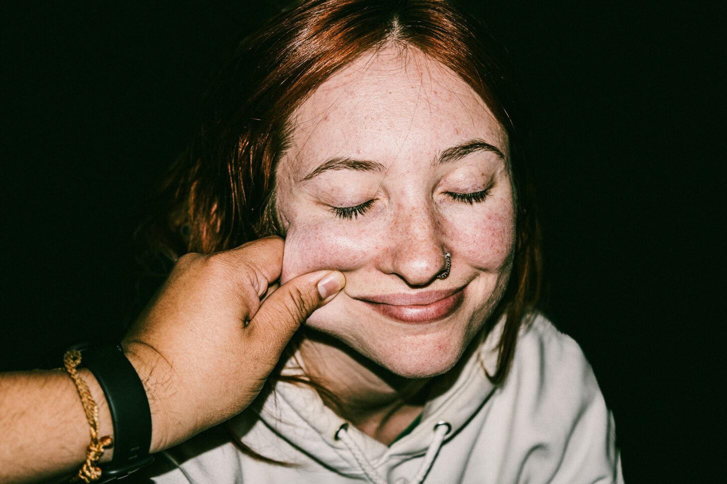 A woman with a bright, surprised smile and raised eyebrows in a flash-lit portrait, part of the 'Cheeky Bastards' reaction series.