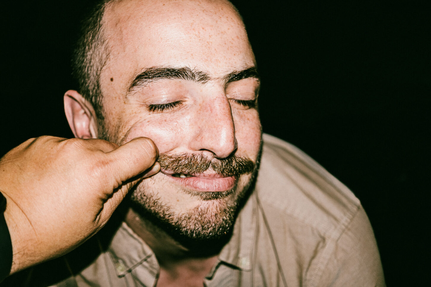 A subject gently pushing the pinching hand away while laughing in a candid, action-filled 'Cheeky Bastards' shot.