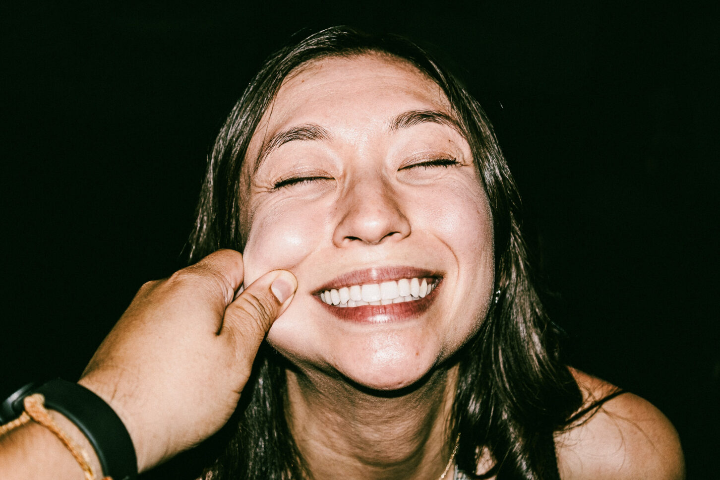 A woman with a bright, surprised smile and raised eyebrows in a flash-lit portrait, part of the 'Cheeky Bastards' reaction series.