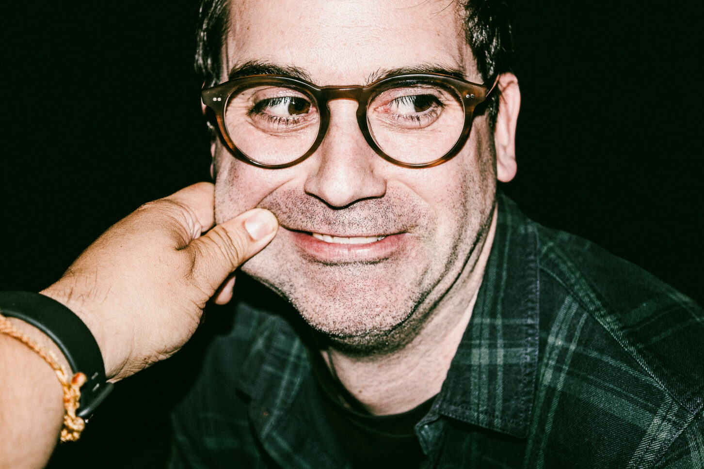 A subject with a confused, furrowed brow in a raw street-style portrait, enduring a left-cheek pinch for the 'Cheeky Bastards' art series.