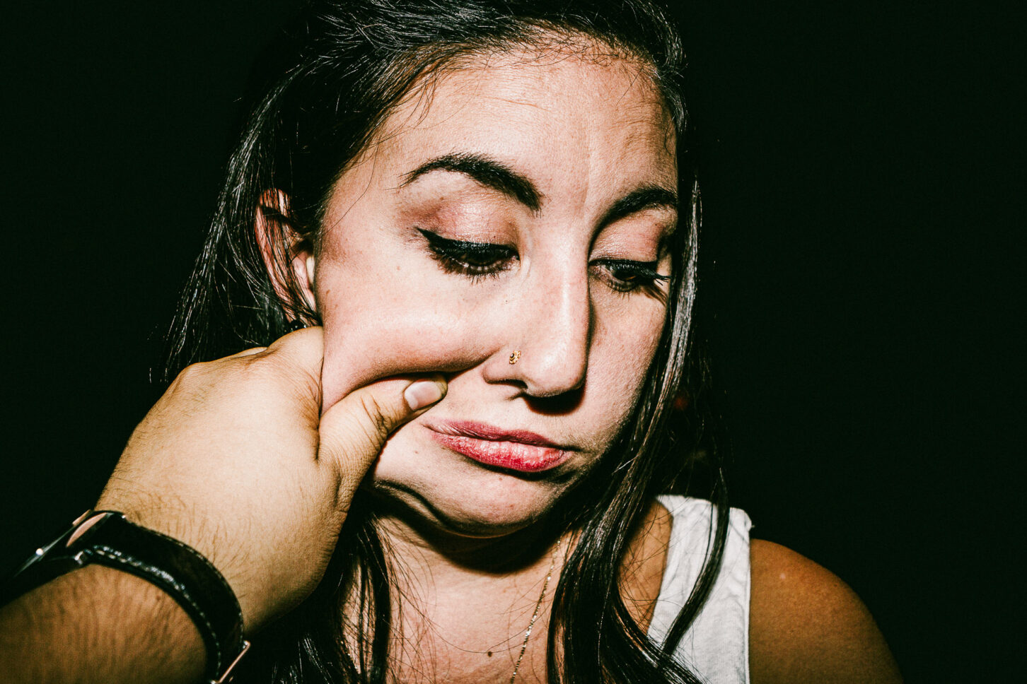 A moody, high-contrast shot of a subject looking down while enduring a cheek pinch, adding a different tone to the 'Cheeky Bastards' series.