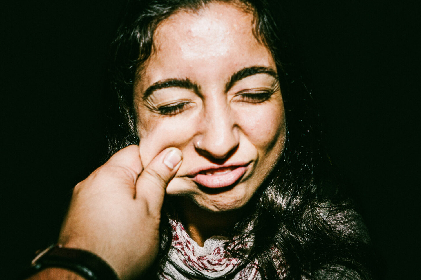 A person with a "painfully funny" grimace, eyes squeezed shut, in a raw flash portrait reacting to the 'Cheeky Bastards' pinch.