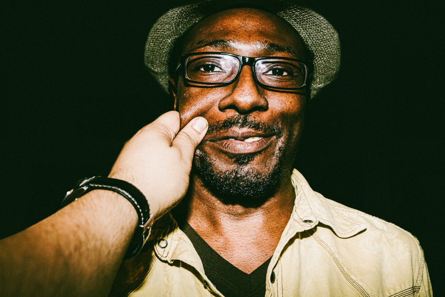 A person looking directly into the lens with an intense, wide-eyed stare while their cheek is pinched, highlighting the raw energy of the 'Cheeky Bastards' series.