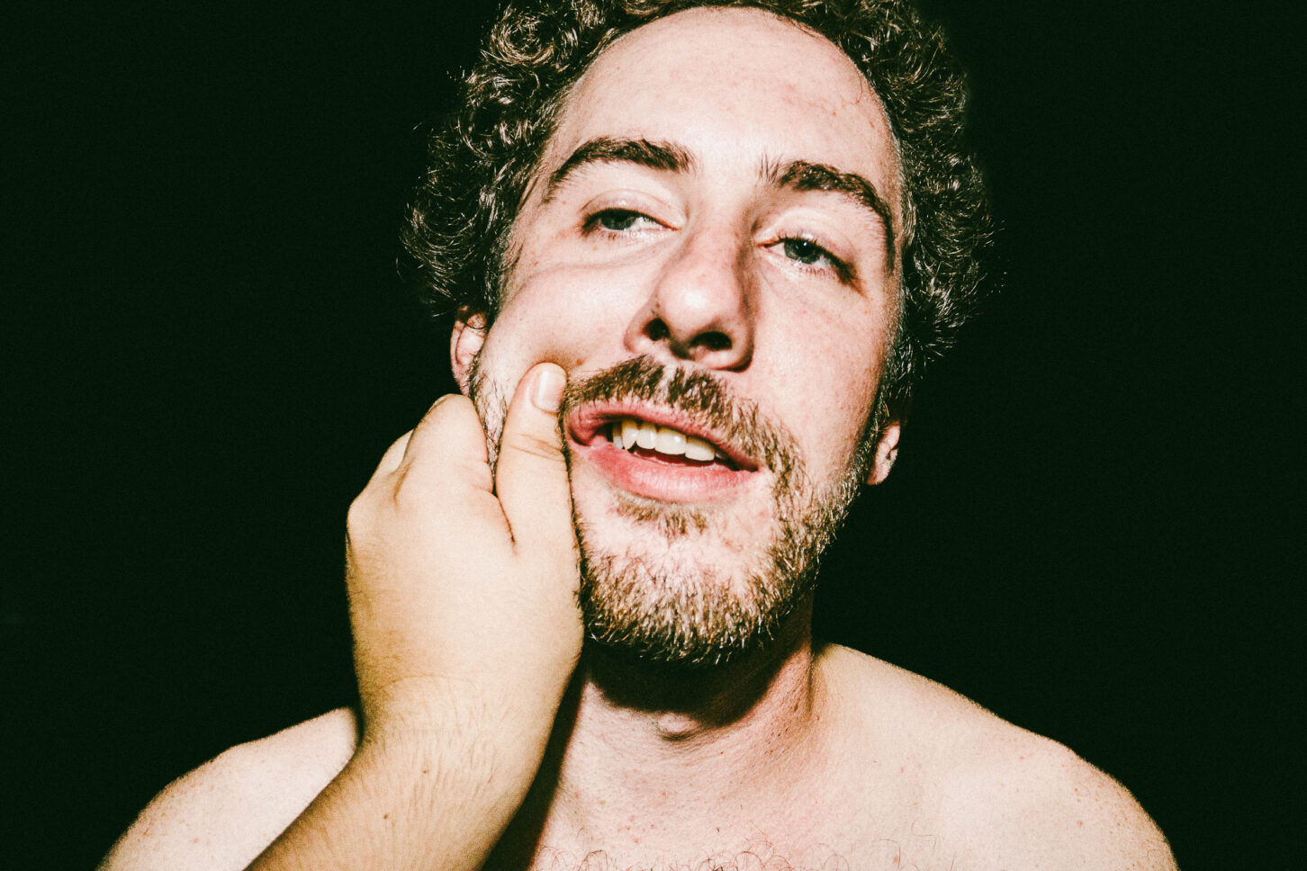 A candid profile shot of a subject turning away while laughing, captured with a harsh flash during a 'Cheeky Bastards' cheek pinch.