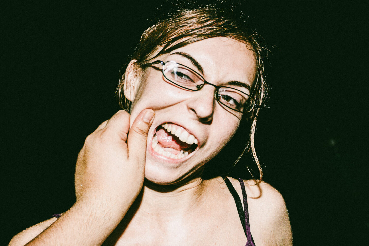 A woman with a bright, surprised smile and raised eyebrows in a flash-lit portrait, part of the 'Cheeky Bastards' reaction series.